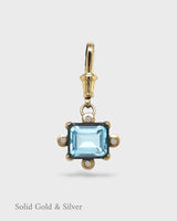 Gold and silver pendant with a blue gemstone on a white background