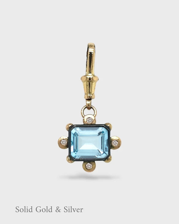 Gold and silver pendant with a blue gemstone on a white background