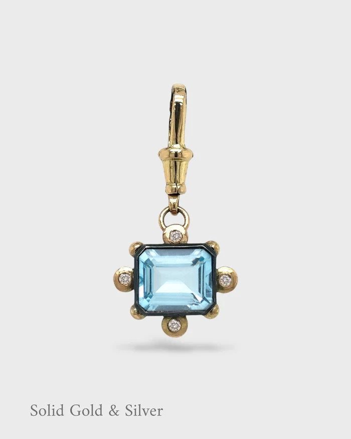 Gold and silver pendant with a blue gemstone on a white background